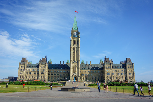 The Canadian Flag flies in full in front of the Parliament of Canada, the Peace Tower is seen in the background on a cloudy day in Ottawa.