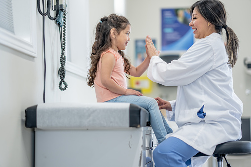 A sweet little girl sits up on an exam table at the doctors as she gives her doctor a High Five after a good report.