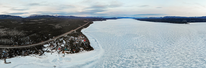 Spring time panoramic view in northern Canada with snow capped mountains over the Yukon River. Taken from drone, aerial view with frozen lake and ice covering the body of water in scenic views.