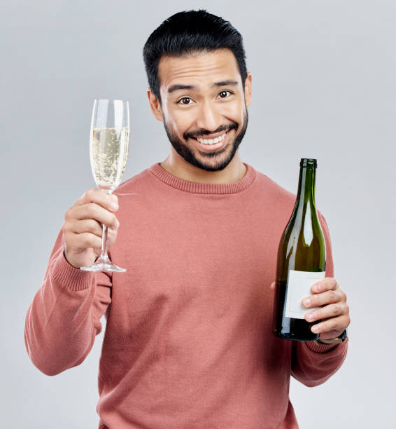 porträt, champagner und toast mit einem mann im studio auf grauem hintergrund, der eine flasche zur feier hält. glas, alkohol und prost mit einem gutaussehenden jungen mann, der die neujahrstradition feiert - flute solo stock-fotos und bilder