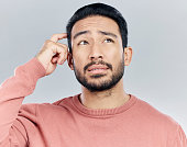 Thinking, confused and doubt with a man in studio on a gray background looking thoughtful or contemplative. Question, idea and memory with a young asian male trying to remember but feeling unsure