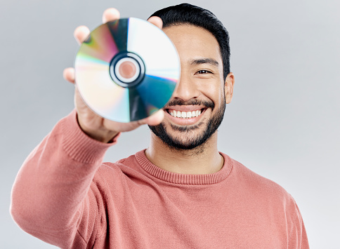 Man, holding and compact disc in studio portrait for smile, happiness and technology by white background. Asian model, student and cd in hand for movie, audio and sound with happy, excited and tech