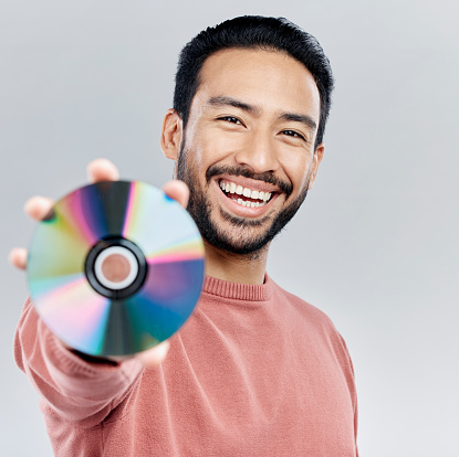 Happy, showing and portrait of an Asian man with a cd isolated on a white background in a studio. Smile, excited and a Japanese person with a copy of multimedia, music or a movie on a backdrop