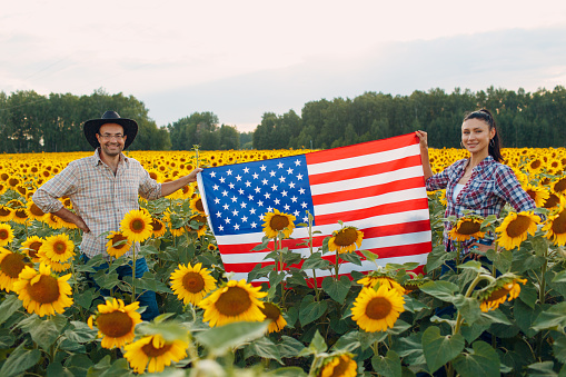 Man and woman farmers at sunflower field with american flag.