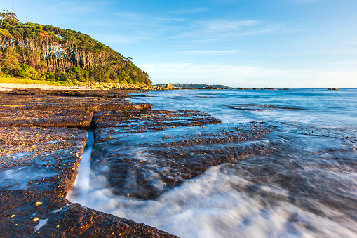 Waves washing gently over rocks on a summers day with clear blue sky. Photographed on South Coast, NSW, Australia.