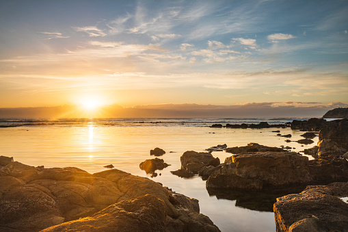 Tidal pools by the ocean reflecting a golden sunrise. Mollymook, South Coast, NSW, Australia