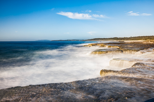 Waves washing gently over rocks on a summers day with clear blue sky. Photographed on South Coast, NSW, Australia.