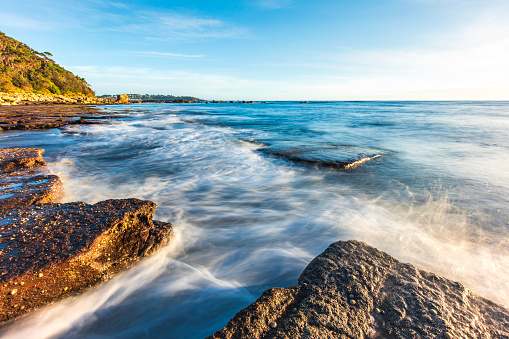 Waves washing gently over rocks on a summers day with clear blue sky. Photographed on South Coast, NSW, Australia.