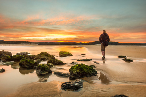 Young man walking across sandbar toward beautiful sunset. Photographed on South Coast of NSW, Australia.