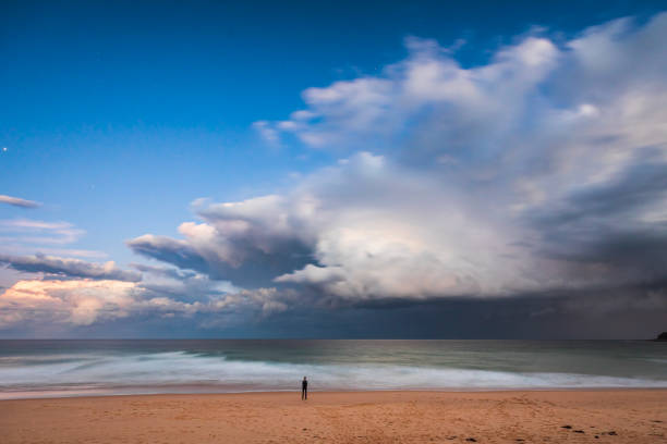 Lone man watching a dramatic storm cloud system over the ocean coming in to coast. South Coast, NSW, Australia.