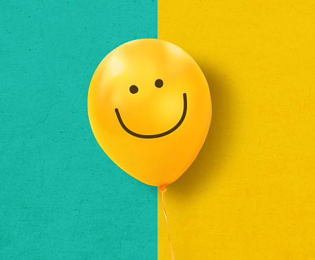 Yellow balloon with smile on blue and yellow texture background. Concept of positive thinking
