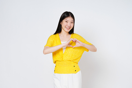 Smilling woman doing a heart shaped gesture with her fingers isolated on white background.