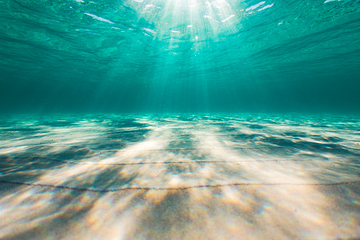 Underwater sun light rays in clear ocean water and sandy bottom.