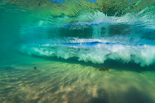 Underwater view of vortex in wave breaking in pristine clear ocean water and sandy bottom.