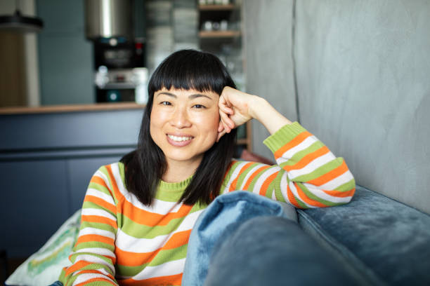 istock Young Japanese woman smiling while sitting on a couch and looking at the camera 1496539235
