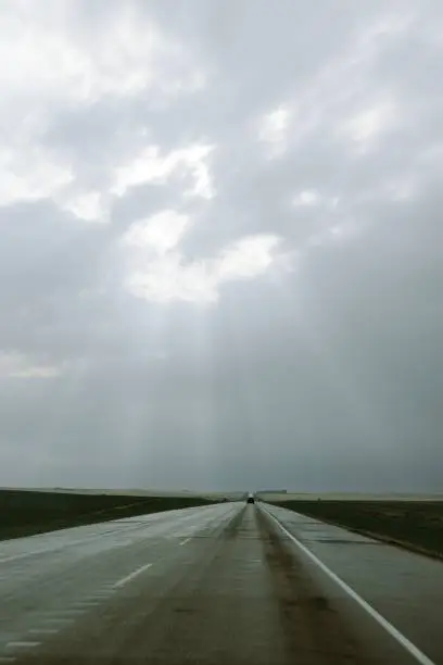 Photo of Grey, cloudy sky looms overhead, casting a shadow over the road and surrounding meadow