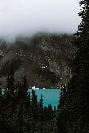 An awe-inspiring view of a mountain shrouded in a thick fog, surrounded by a tranquil blue lake.