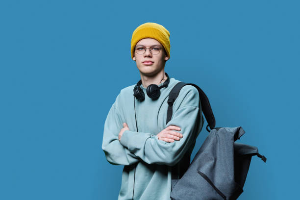 istock Young male in yellow cap sweatshirt with headphones backpack on blue background 1496540964