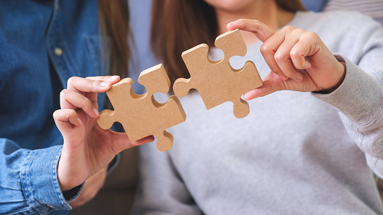 Closeup image of a couple women holding and putting a piece of wooden jigsaw puzzle together