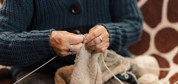 Abuela en la sala de casa feliz y concentrada, usando unos palitos de tejer y lana de oveja, concepto de vida cotidiana tradicional, tejedora tradicional, enfoque selectivo. Dia de los abuelos