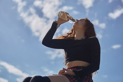 Young adult female athlete drinks water after a ride in a skate park