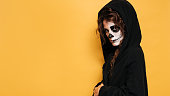 A young woman in a hood with scary makeup. on a yellow isolated background. Concert costume party. A place for your text, advertising. Banner.