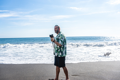 Photo with copy space of a man carrying a digital camera on a tropical beach
