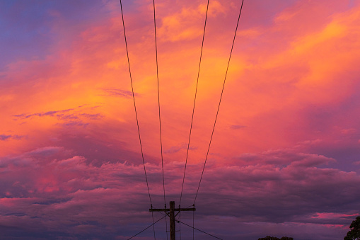 Powerlines against a dramatic cloudscape illuminated by the sunset.