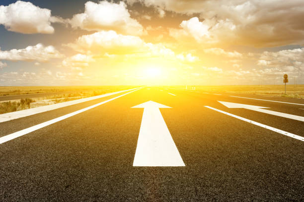 The ahead arrow on the asphalt road and sunset background