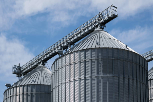 Steel grain storage silos with a conical bottom can be used for various purposes. Industrial facilities of feed and flour mills. Against the backdrop of a beautiful sky with clouds.