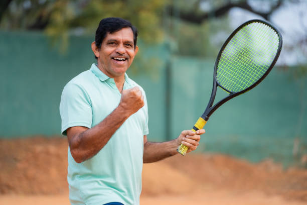 indyjski senior świętujący zwycięstwo patrząc kamerą za punktem podczas gry w tenisa - koncepcja rywalizacji, energicznego i fitness stylu życia. - tennis men vitality joy zdjęcia i obrazy z banku zdjęć