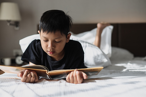 Asian kid lying at the bedroom and reading book