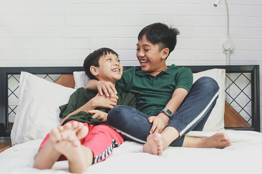 Asian young brothers relax in the bedroom, smiling and embrace each other.