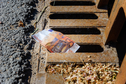 Eu 50 euro banknote down the street storm drain. Concept of senseless waste of money, loss, useless waste.