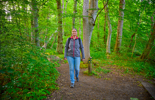 Mid adult woman trekking in Danish nature. Summertime front view full length portrait.