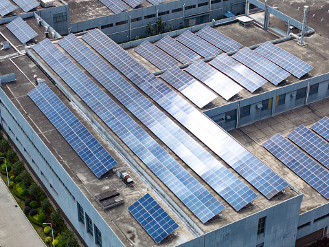 Production of sustainable energy. Aerial view of solar power plant with blue photovoltaic panels mounted on industrial building roof for producing green ecological electricity.