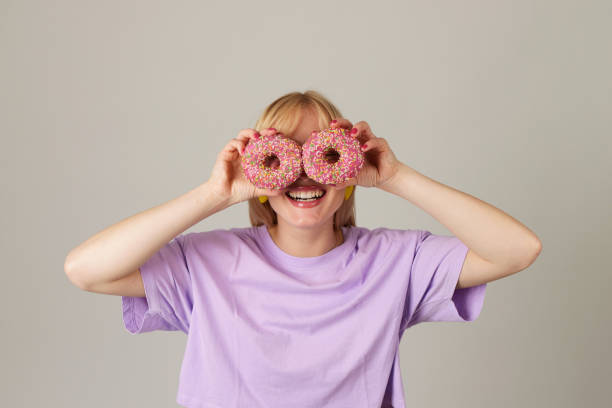 istock Smiling young woman holding donuts with pink icing against her eyes 1496568515