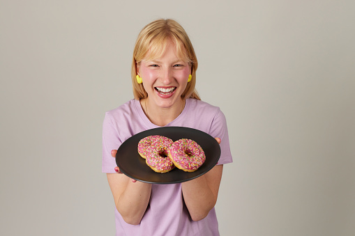 Beautiful young woman smiling, holding a plate full of delicious color donuts