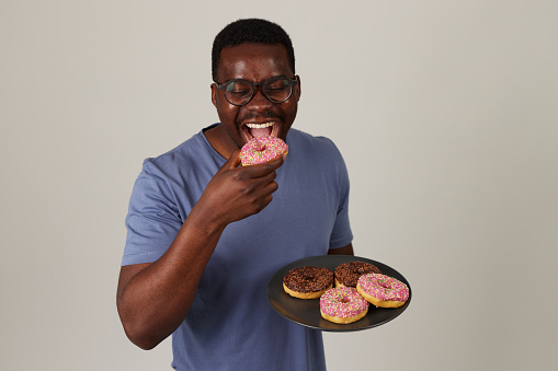 Smiling young man holding a plate full of delicious donuts against grey background