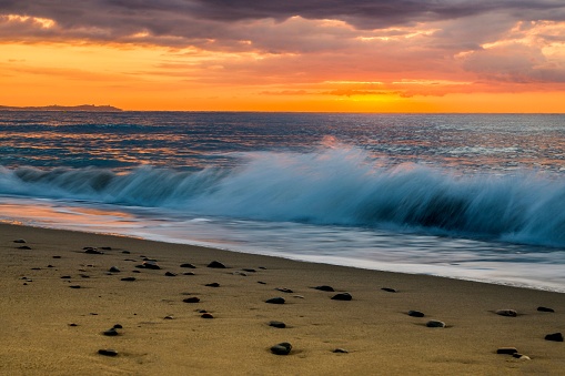 A wave-lashed shore at dawn silhouetted against a vibrant sunrise.