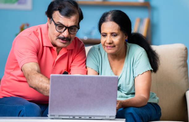 istock Indian senior couple discussing by watching laptop while sitting on sofa at home - concept of technology, communication and bonding 1496571257