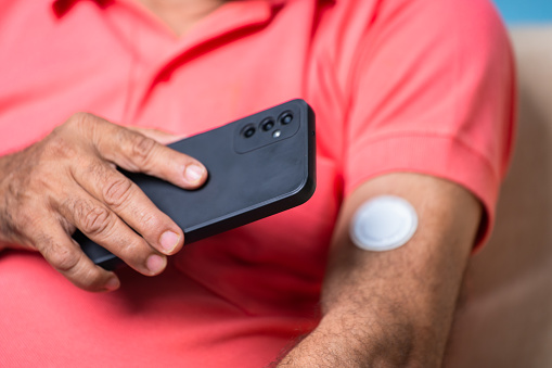 Close up shot of senior man checking sugar or glucose level by tapping mobile phone to sensor at home - concept of technology, diabetes and health care.