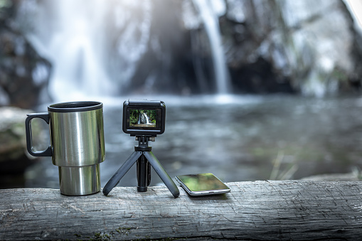 action camera,coffee cup,mobile phone on wood with the waterfall behind.