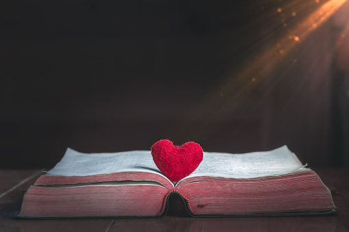 Corazón rojo sobre la biblia sobre una mesa de madera Con luz de la mañana, de cerca, amor al concepto cristiano. photo
