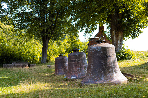 A large, weathered bronze bell stands tall and majestic against the backdrop of a clear, vibrant blue sky.