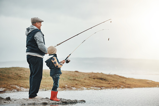 Lake, travel and grandfather fishing with a kid while on a adventure, holiday or weekend trip. Hobby, outdoor and elderly man teaching a child to catch fish in nature while on vacation in countryside