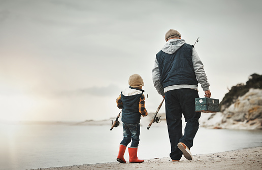 Walking, back and child with grandfather for fishing, bonding and learning to catch fish at the beach. Morning, holiday and boy on a walk by the sea with an elderly man to learn a new hobby together