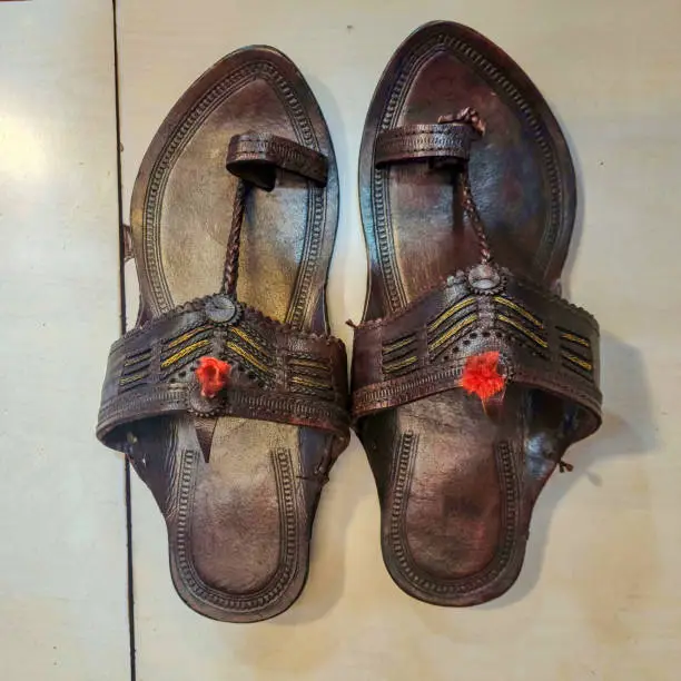 Photo of Stock photo of popular and traditional dark brown color handmade kolhapuri chappal for men, Picture captured under bright light at Kolhapur, Maharashtra, India. white color marble floor on background