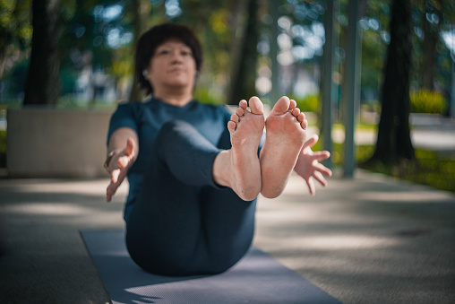 asian chinese mature woman practicing yoga in public park during weekend morning