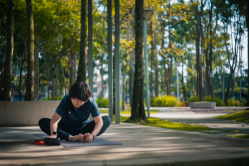 Asian Chinese mature woman watching video from smartphone virtual yoga class in public park